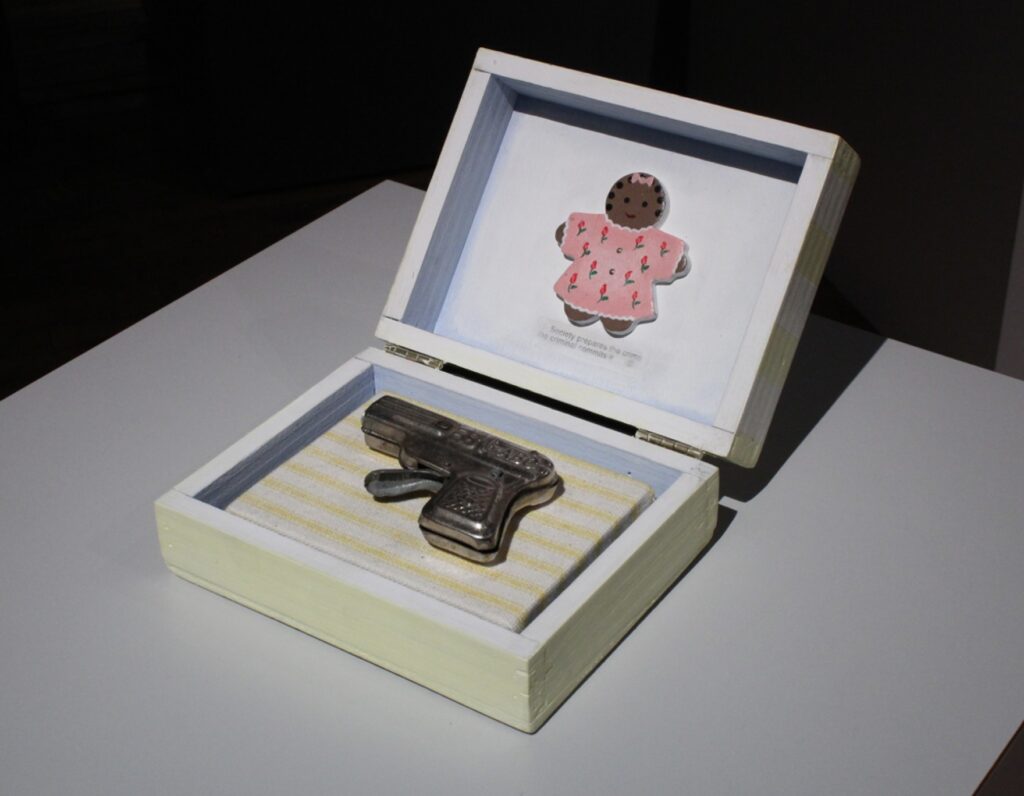 Image: Renée Stout. "Baby’s First Gun," 1998. The piece is comprised of an opened box with a small gun inside and a gingerbread-shaped little girl displayed on the inside of the lid. Courtesy of Belger Arts Center, Kansas City, MO.
