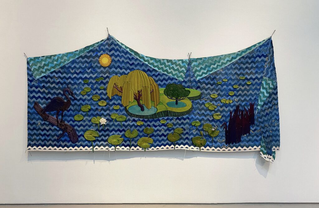 Image: Dan Gunn, Wetland Scenery, 2021, acrylic, milk paint, light stable metalized acid dye, polyurethane on birch plywood and poplar with nylon cord. Photo by Ely Maris. An installation view of a textile piece hanging on a white gallery wall. The piece depicts a wetland scene of waterlilies sitting on water with reeds to the right, a heron to the left, and trees and a sun in the background.