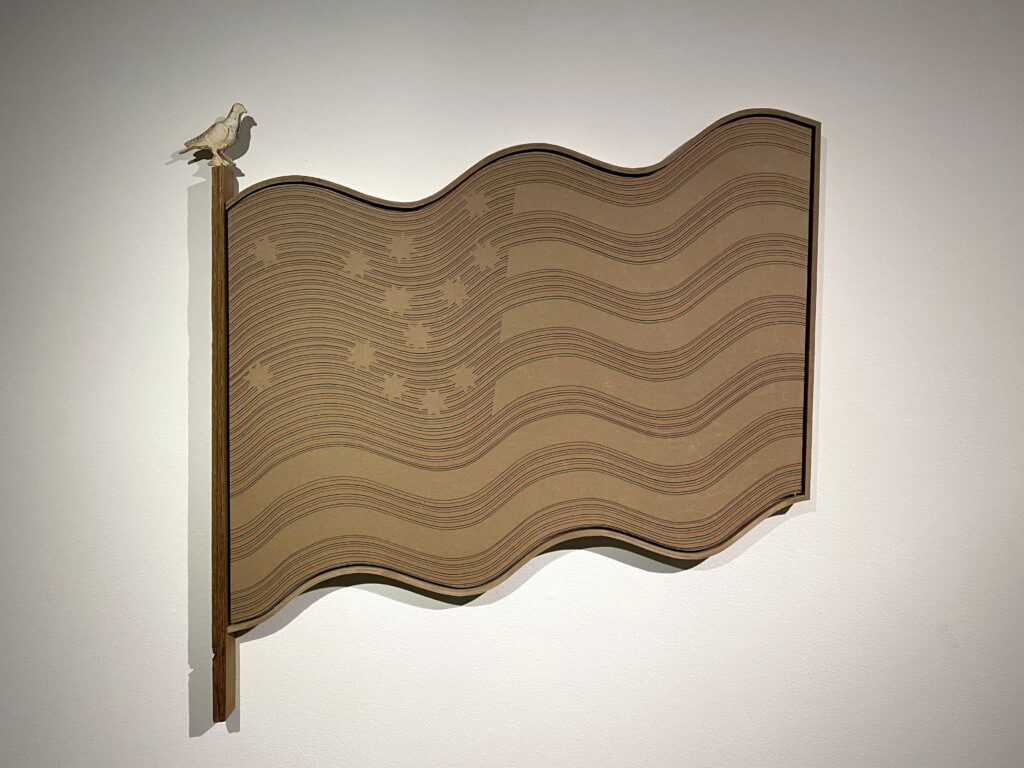 Image: Lyndon Barrois Jr., Brown Paper Flag Test, 2017, ink, butcher paper, laser print, enamel pin, chipboard, and cedar frame, 24" x 42". Photo by Ely Maris. An installation view of a constructed American flag hanging on a white wall. The flag is all brown, the color of a brown paper bag.