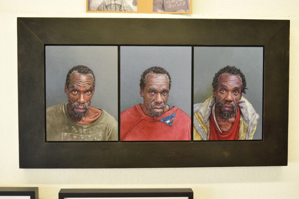 Image: Dick Dougherty, Arrested: (Camping Prohibited) Roger in Three Panels, oil on linen covered panels, each image 9” x 12”. Three paintings of portraits of a man looking straight at the camera for three separate mug shots. She has short black hair, a beard, and wears (from left to right) a green shirt, a red sweater, and a yellow coat. Photo by Kim Kobersmith.
