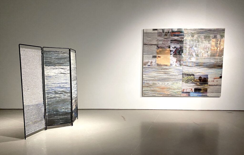 Image: Margo Wolowiec: (L) 11 Cities, handwoven polymer, linen, dye sublimation ink, acrylic paint, indigo dye, reflective mylar from emergency preparedness kits, hot rolled steel, 70" x 66". (R) Wandering Path, 2021, handwoven polymer, linen, dye sublimation ink, acrylic paint, deadstock organic cotton, reflective mylar from emergency preparedness kits, sterling silver-leafed thread, 45" x 52". Photo by Ely Maris. Two artwork are installed in a gallery. The one on the left is in the shape of a partition and shows water, the one on right shows a variety of imagery.