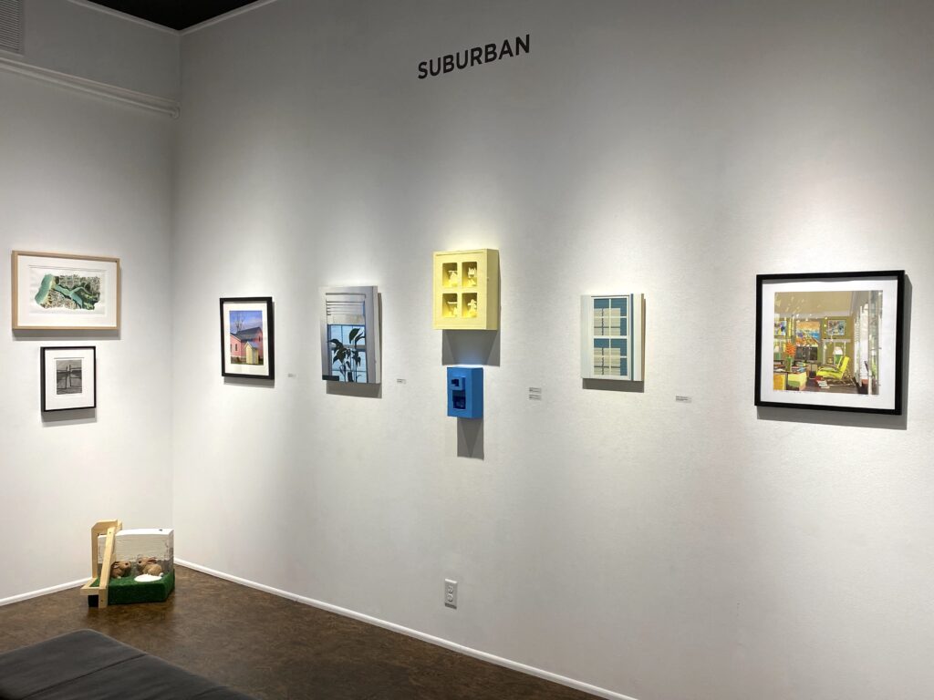 Image: A view of the exhibition Suburban at Manifest Gallery. A variety of different artworks hang on the gallery wall. From left to right, the works are by Richard J. Diedrich, Tyler Thenikl, Roscoe Wilson, Chris Offutt, Brooks Cashbaugh, James Wade, Maddie Aunger, and Stephen Yuen. Photo by the author.