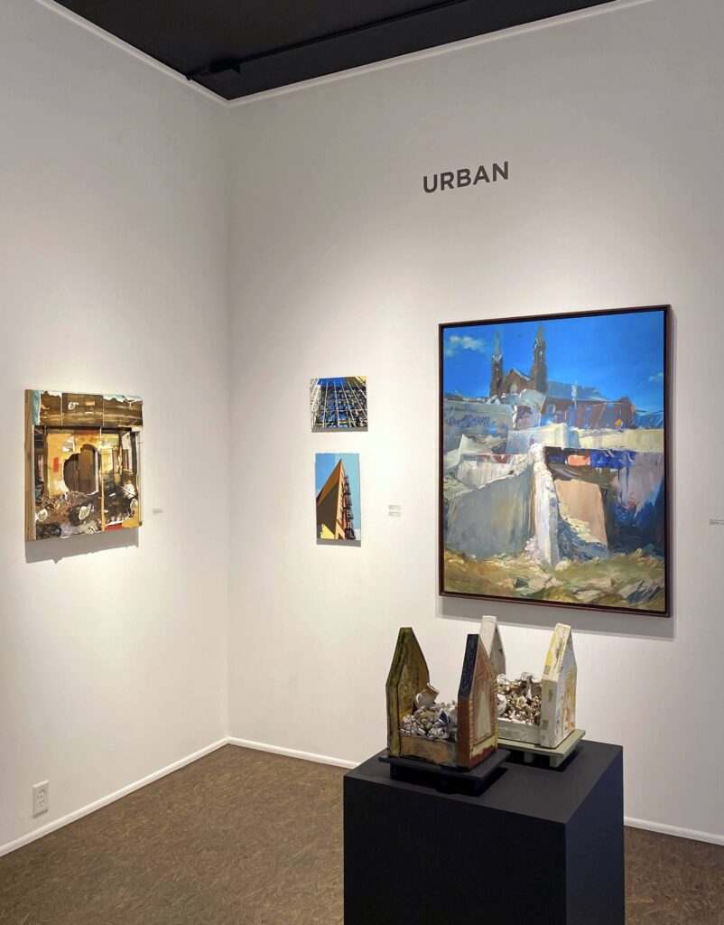 Image: A view of the exhibition Urban at Manifest Gallery. A variety of different artworks hang on the gallery wall. A sculpture sits on display on a pedestal in the foreground. From left to right, the works are by Dereck Mangus, John Ferry, Marlene Steele, and Lydia Thompson. Photo by the author.