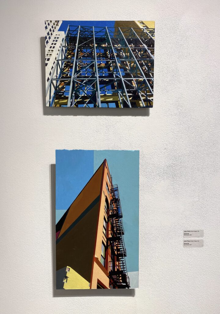 Image: Two colorful, architectural paintings hang on a white wall. Top: John Ferry, Detroit #1, 2021, oil on board. Bottom: Detroit #2, 2021, oil on board. Photo of artworks by the author.