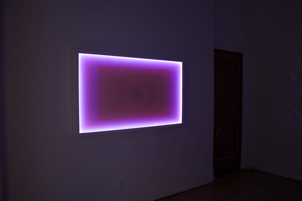 Image: An installation view of A Thought is a River, curated by John Knuth. Letitia Quesenberry, Hyperspace 37, 2020, wood, lacquer, LED, acrylic, 36" x 60" x 3". A magenta, rectangle-shaped piece glows on display in a dark room. Photo by CM Turner.