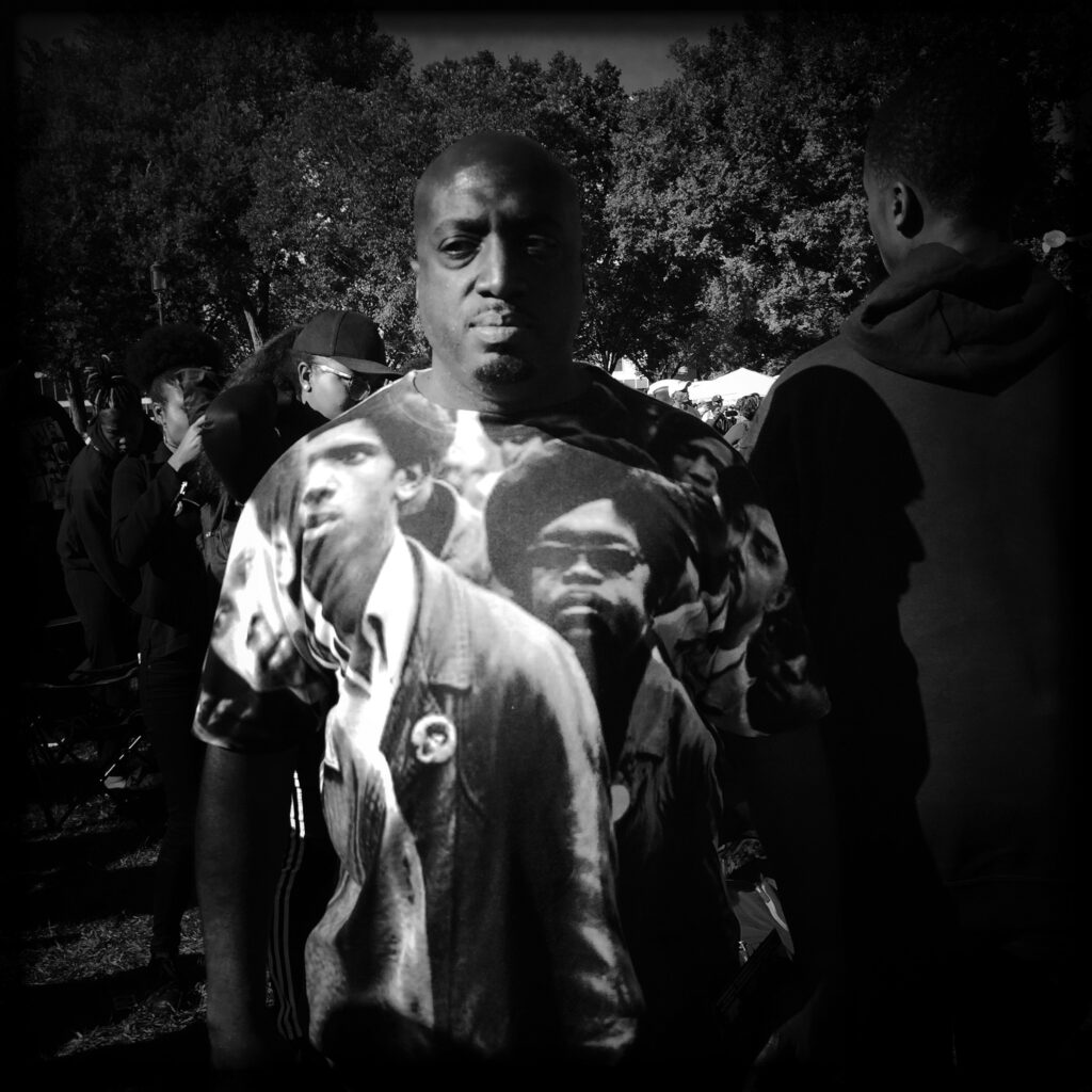 Image: A black and white photo by Carlos Javier Ortiz. Ortiz: "Thousands gather on the Mall in Washington D.C on Saturday for the 'Justice or Else' rally. Black men and woman and from different races from across the country gathered for the Million Man March in Washington D.C., led by Nation of Islam leader Louis Farrakhan, on Saturday October 10, 2016. This year marks the 20th anniversary of Million Man March in Washington, D.C. The 20th anniversary of the March calls for a renew call for justice." The photo shows a Black man in a crowd facing the viewer. Image courtesy of Carlos Javier Ortiz.