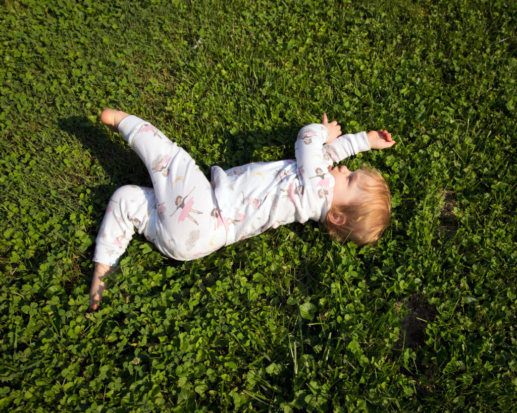 Image: A color photograph of a small child sprawled out on a patch of green clovers. © Rachael Banks. Images courtesy of the artist.