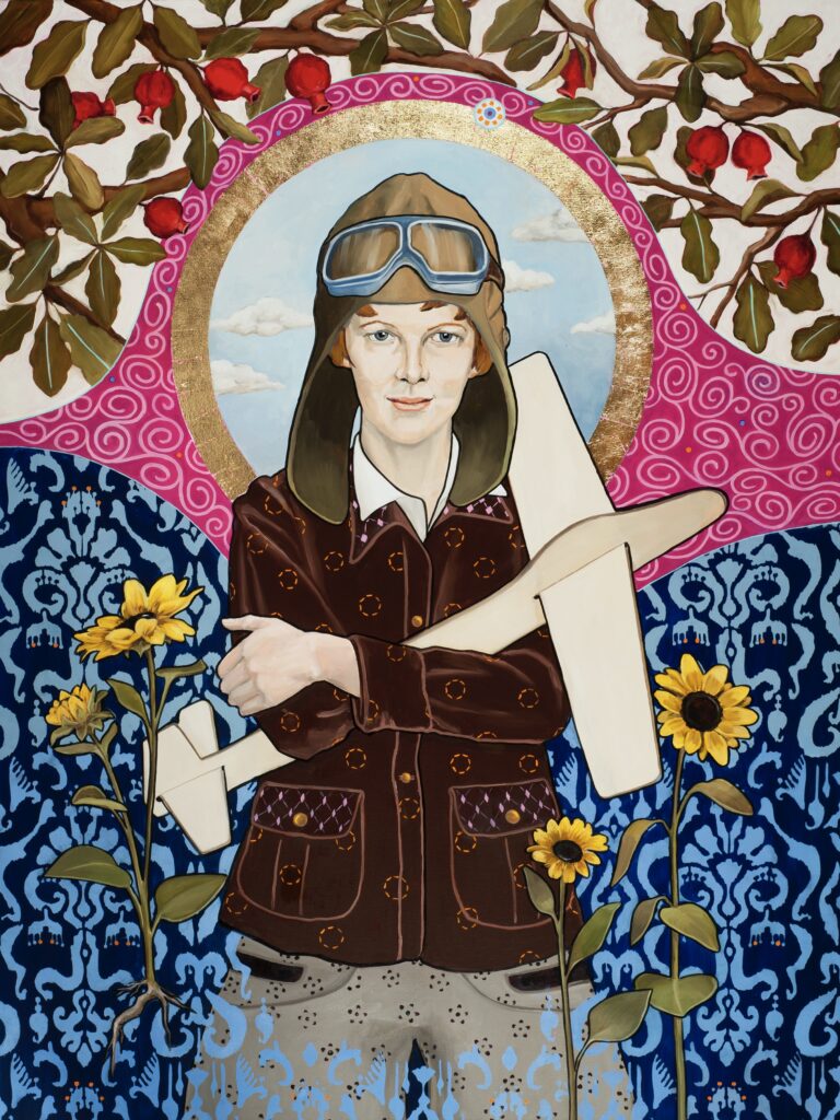 Image: Honora Jacob, Amelia’s High Flying Dream, 2022, oil and gold leaf on canvas, 48” x 36”. A painting depicting Amelia Earhart standing looking directly at the viewer. She is wearing a pilot's cap and jacket with her arms crossed. In her arms is a toy airplane. The background shows various floral patterns and a gold halo-like circle is behind Amelia's head. Image courtesy of the artist. 