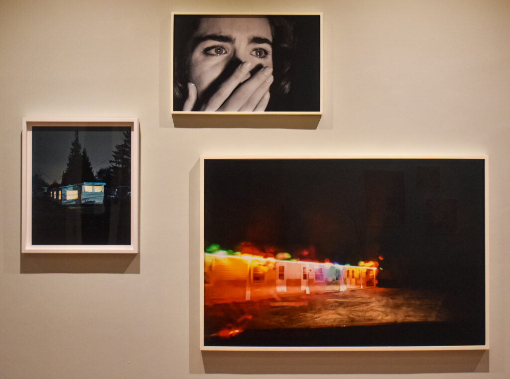 Image: Todd Hido, three untitled images. The images at left and lower right are from the artist's Homes at Night series, pigment C-print. The image at top: monochromatic C-print. The two pieces at the bottom depict homes lit up from the inside during a dark night. The image at the top depicts a close up of a person's face with their hand covering their mouth. Photo by Kevin Nance.
