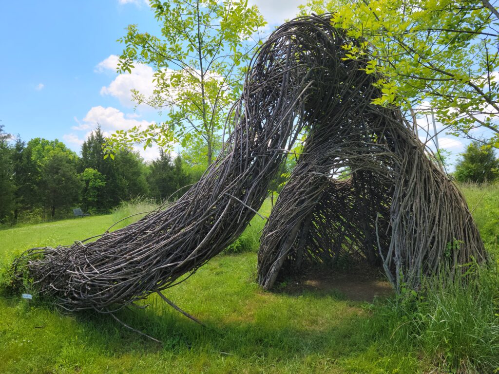 Image: Sounds of the Whippoorwill by Justin Roberts. A photo of a sculpture that appears to be made from twisted twigs. The sculpture creates a structure that visitors can enter.