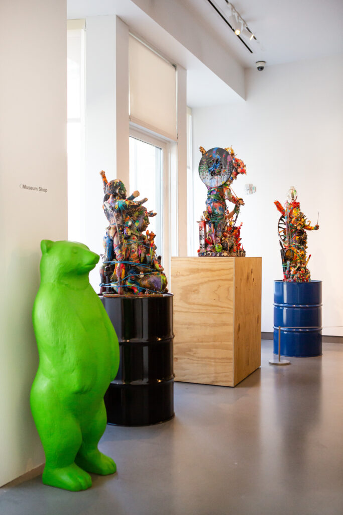 Image: Robert Morgan, Bodhi Tree, 2017, Island of Lost Souls, 2011, Electric Lady Land, 2018. All Mixed Media. An installation view of Robert Morgan's exhibition at 21c Lexington. Three colorful mixed-media sculptures sit atop pedestals along a wall. In the foreground is a neon green bear sculpture. Image courtesy of 21c Lexington.