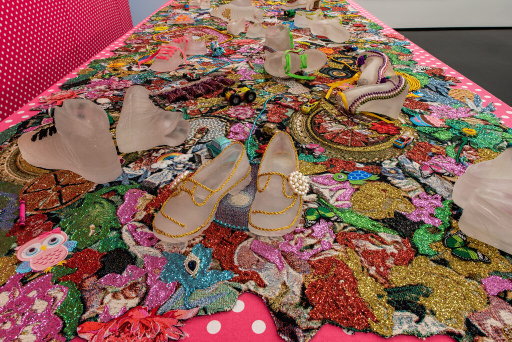 Image: Detail shot of Ebony G. Patterson, …and babies too…, 2016-2018. Jacquard woven photo tapestry with digitally embroidered appliques, hand-embellished cast glass shoes, and toys; fabric covered papier-mâché balloons 45.6” x 163.2” x 60”. Courtesy of the artist and Monique Meloche Gallery.