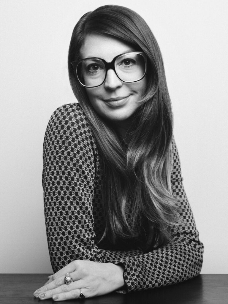 Image: A black and white photo of Bridget Finn. She is leaning on a table while looking forward into the camera. Photo by Dustin Aksland.