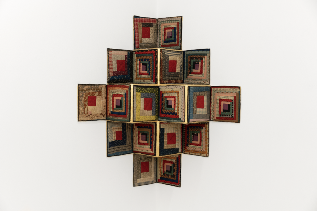 Image: Sanford Biggers, Fool's Gambit, 2019. Antique quilt, birch plywood, gold leaf. 39.75 x 35.75 in, ssbobj339. Courtesy of David Castillo Gallery. Photographed by Zachary Balber. A photograph of a quilt piece made of geometric tans, golds, reds, and dark blues. The piece is constructed onto wood so that it takes a three-dimensional shape.