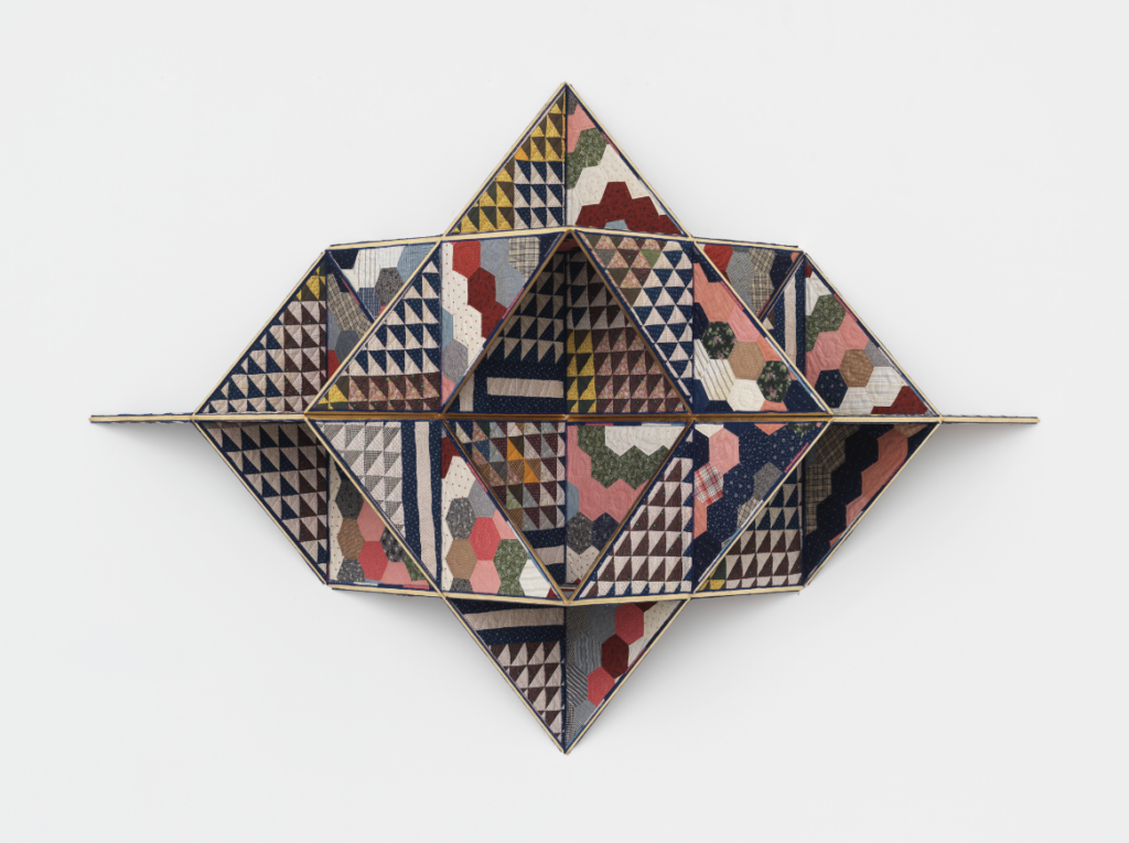 Image: Sanford Biggers, Khemetstry, 2017. Antique quilt, birch plywood, gold leaf, ssbobj167. © Sanford Biggers and Marianne Boesky Gallery. Photography by Object Studies. A photograph of a quilt piece made of mostly primary colors in geometric shapes. The piece is constructed onto wood so that it takes a three-dimensional shape.