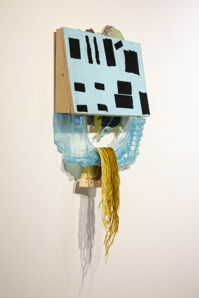 Image: Ogygia Filled with Wings by Lisa Bachman Jones. A mixed media, sculptural piece hangs on a gallery wall. The piece is mostly made up of shades of blue and yellow, with squares of black on the top half. Photo by Annaliese Loughead, courtesy of The Parthenon Gallery.